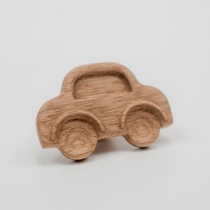 Könnte beinhalten: Ein Holzspielzeugauto im klassischen Design. Das Auto besteht aus hellbraunem Holz mit abgerundeten Kanten und sichtbarer Holzmaserung. Es hat vier Räder und ein gewölbtes Dach, ideal für Kinder.