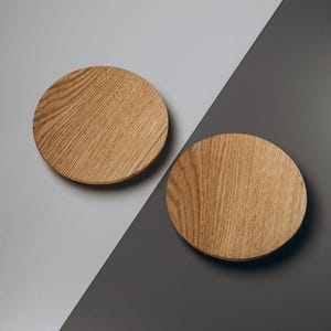 May include: Two round wooden plates with a natural wood grain pattern. The plates are light brown and sit on a diagonal background of gray and dark gray. The plates are likely for serving food or as decorative items.