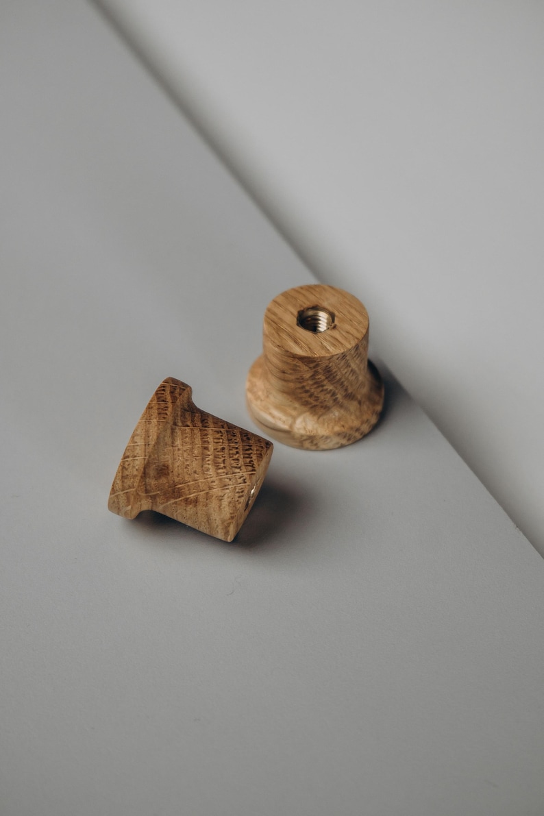 Peut inclure: Deux boutons de meuble en bois avec une finition naturelle vein&eacute;e. L'un des boutons est couch&eacute; sur le c&ocirc;t&eacute;, tandis que l'autre est debout. Les deux boutons ont un insert filet&eacute; pour une installation facile. Les boutons sont pos&eacute;s sur un fond gris.