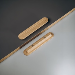 May include: Two light-colored wooden magnetic poster hangers. One is a long, thin strip, and the other two are rectangular with rounded edges. The background is divided diagonally into gray and light gray sections.