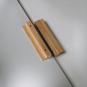 May include: Two wooden magnetic poster hangers. One hanger has a groove and a small metal screw. The other is a plain wooden bar. Both are made of light-colored wood and are on a gray background.