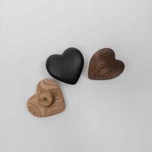 May include: Three heart-shaped wooden knobs in varying shades of brown and black. One is a light wood with a brass screw, another is a dark brown, and the third is black. These decorative knobs are ideal for furniture.
