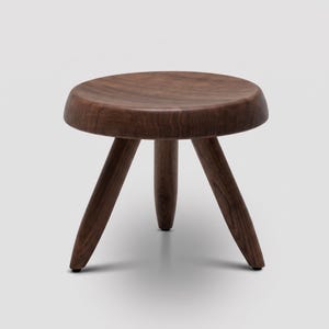 Könnte beinhalten: Ein kleiner, runder Hocker aus dunkelbraunem Holz mit einer glatten, polierten Oberfläche und drei stabilen, konisch zulaufenden Beinen. Der Hocker weist eine sichtbare natürliche Holzmaserung auf dem runden Sitz und den Beinen auf.