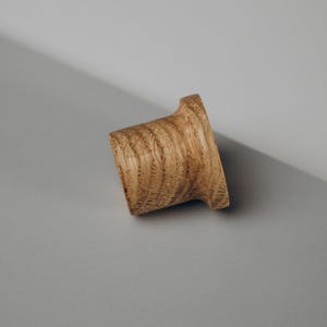 Peut inclure: Un bouchon de bouteille en bois avec une base &eacute;vas&eacute;e et un corps cylindrique incurv&eacute;. Le bouchon est en bois brun clair avec des motifs de grain visibles. Le design est simple et &eacute;l&eacute;gant, adapt&eacute; aux bouteilles de vin.