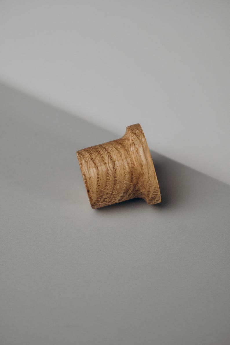 Peut inclure: Un bouchon de bouteille en bois avec une base &eacute;vas&eacute;e et un corps cylindrique incurv&eacute;. Le bouchon est en bois brun clair avec des motifs de grain visibles. Le design est simple et &eacute;l&eacute;gant, adapt&eacute; aux bouteilles de vin.