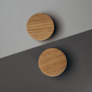 Peut inclure: Deux boutons de meuble ronds en bois clair, avec un grain naturel. Ils sont plac&eacute;s sur un fond diagonal, avec une partie sup&eacute;rieure grise et une partie inf&eacute;rieure gris fonc&eacute;.