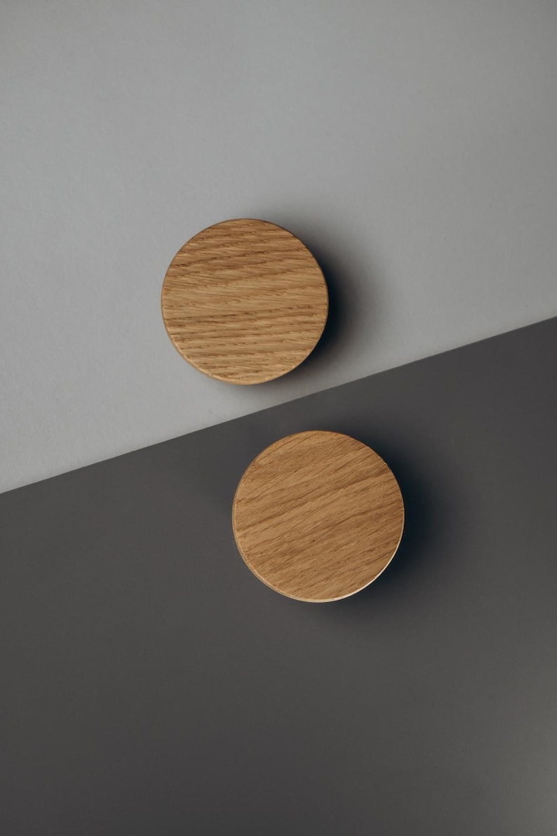 Peut inclure: Deux boutons de meuble ronds en bois clair, avec un grain naturel. Ils sont plac&eacute;s sur un fond diagonal, avec une partie sup&eacute;rieure grise et une partie inf&eacute;rieure gris fonc&eacute;.