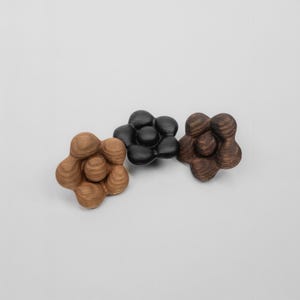 May include: Three wooden flower-shaped decorative objects. One is light brown, one is black, and the other is dark brown. Each has a unique, organic design with rounded, textured surfaces. The objects are arranged on a plain white background.