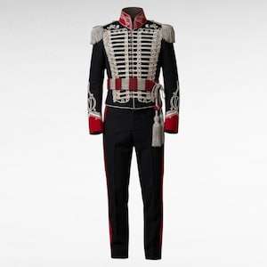 Peut inclure: Un ensemble d'uniforme militaire noir comprenant une veste avec des détails de cordons tressés blancs, des boutons argentés et des poignets rouges. La veste présente des épaulettes à franges et une ceinture rouge et blanche à pompons.