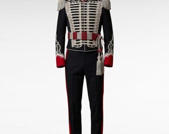 May include: A black military-style uniform set featuring a jacket with white braided cord detailing, silver buttons, and red cuffs. The jacket includes shoulder epaulets with fringe, and a matching red and white sash with hanging tassels.
