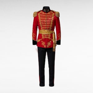 Peut inclure: Une veste de style militaire rouge ornée de cordons tressés dorés, de boutons dorés et d'épaulettes à franges. La veste comprend une ceinture dorée à pompons et est assortie d'un pantalon noir avec une fine bande rouge sur le côté.