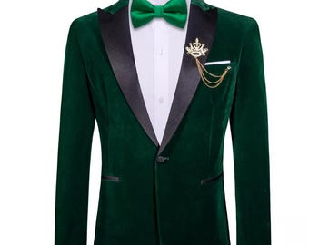 May include: A dark green velvet blazer with a black satin lapel, a white dress shirt, and a green bow tie. The blazer has a gold-colored crown pin with a chain. The blazer has a single-button closure and a pocket square.