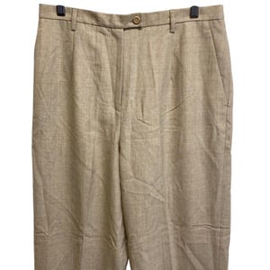 Op de afbeelding: Beige broek met knoopsluiting en riemlussen. De broek is gemaakt van een geweven stof en heeft een klassiek, op maat gemaakt ontwerp. De broek wordt gepresenteerd op een zwarte hanger.