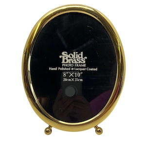 May include: Oval solid brass photo frame. The frame is hand polished and lacquer coated. The frame is 8" x 10" and has a black interior. The frame has two small ball feet.