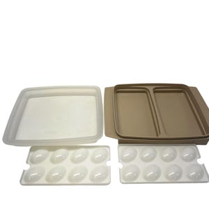 Pode incluir: Uma coleção de recipientes de plástico para armazenamento de alimentos. Inclui um recipiente retangular transparente com tampa, uma bandeja dividida bege e duas bandejas brancas em forma de ovo, cada uma com oito moldes em forma de ovo. Ideal para organização da cozinha.