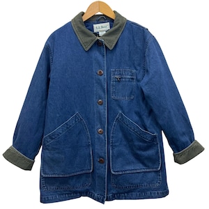 Puede incluir: Chaqueta vaquera azul con cuello y puños de pana verde. La chaqueta tiene cuatro bolsillos grandes, botones marrones y el logo "L.L. Bean" en el cuello. Cuelga de una percha de madera.
