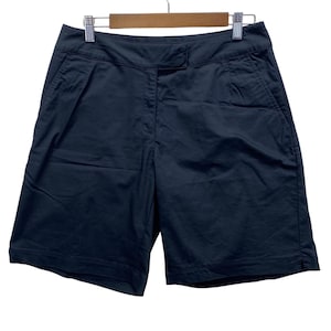 Op de afbeelding: Marineblauwe shorts hangen aan een houten hanger. De shorts hebben een knoopsluiting, zakken en een getailleerd ontwerp. De shorts zijn gemaakt van een lichte stof, geschikt voor warm weer. De shorts zijn ongeveer 46 cm lang.