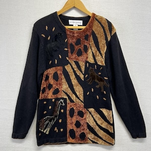 May include: Black long-sleeve sweater with a patchwork design featuring animal appliqués. The sweater has a crew neck and the brand name "VICTORIA HARBOUR" is visible. The design includes brown and tan animal shapes and patterns.