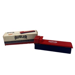 Könnte beinhalten: Rote und schwarze Bugler Premium Filter Zigarettenmaschine mit Originalverpackung. Die Schachtel ist beige mit rotem und schwarzem Text, einschließlich des Markennamens "Bugler". Die Maschine ist rot mit schwarzem Sockel.