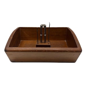 May include: A rectangular wooden nut bowl with a built-in holder for nutcrackers and picks. The bowl is a warm brown color, and the tools are silver and dark metal. The bowl has a curved edge.