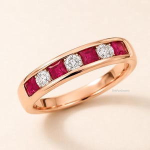 Peut inclure: Une bague en or rose avec un sertissage en canal alternant trois rubis rouges taille princesse et deux diamants blancs taille brillant. Le métal présente une finition polie et le texte TheFunJewels est inscrit sur la surface intérieure.