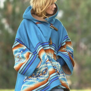 Peut inclure: Un poncho bleu à capuche avec un motif d'inspiration sud-ouest aux tons orange, bleu et crème. Le manteau est doté d'une fermeture à bascule et d'une doublure marron. Les manches ont un design unique et le manteau a des poches.