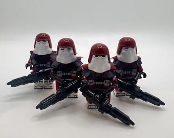 May include: Four Imperial Snowtroopers, each with a red helmet, white face covering, and black and red armor. They are holding black blasters, standing against a white background. These figures are likely part of a collectible set.