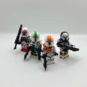 May include: Four Lego clone trooper minifigures in red, green, and orange, each holding a black blaster rifle. The figures have detailed helmets and armor. The background is white.
