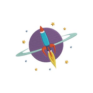 Könnte beinhalten: Gesticktes Design mit einer blau-roten Rakete, die abhebt, umgeben von einem violetten Planeten mit grünem Ring, gelben Sternen und kleinen blauen Kugeln. Das Design befindet sich auf weißem Hintergrund.