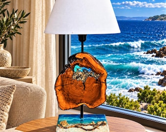 May include: A table lamp featuring a white conical shade, a central vertical black metal rod, and a natural wood slab base with an embedded turquoise resin inlay. The square base mimics a sandy beach with blue resin water and small stones.