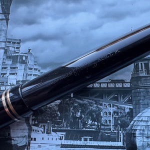 May include: Close-up of a black fountain pen with gold accents. The pen has the text "U.S. PARKER DUOFOLD REG. T. M." engraved on the barrel. The pen is set against a backdrop of a cityscape.