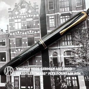 May include: A black Staedtler Mars Flex fountain pen with gold-coloured accents, including a clip and rings. The pen features the text VINTAGE 1930S GERMAN ART DECO STAEDTLER MARS FLEX FOUNTAIN PEN and a circular logo with the letters VPB.