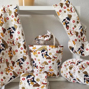Peut inclure: Ensemble d'articles en tissu blanc avec un motif répété de chiens Shiba Inu de différentes couleurs, de fleurs rouges et d'accents dorés. L'ensemble comprend une serviette, une manique, un sac, des dessous de verre et des débarbouillettes.