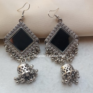 May include: Silver-toned earrings with a geometric design. Each earring features a square black mirror center, surrounded by a decorative border and dangling bell-shaped accents. The earrings have a hook closure.