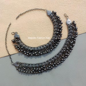 Puede incluir: Dos tobilleras plateadas con diseño de cuentas y cierre de cadena. Las tobilleras presentan una serie de pequeñas cuentas redondas y detalles florales. El texto "Majestic Fashion Hub" es visible.