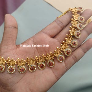 May include: Gold necklace with detailed design. The necklace has circular pendants with red, green, and white gemstones. The text "Majestic Fashion Hub" is visible.