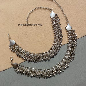 Puede incluir: Dos collares plateados con intrincados diseños de cuentas y extensiones de cadena. Los collares presentan una serie de pequeñas cuentas redondas y elementos decorativos. El texto "Majestic Fashion Hub" es visible.