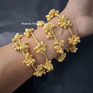 May include: Gold-colored bracelets with a cluster of small, round beads. The bracelets are on a person's wrist. The bracelets have a twisted rope design. The bracelets are a bright gold color.