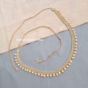 May include: A gold-toned metal waist chain featuring a woven mesh design adorned with small white faux pearls along the bottom edge. The accessory includes a thin adjustable chain with a hook clasp and the text Majestic Fashion Hub.