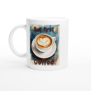 May include: White coffee mug with a watercolour design. The design features a cup of coffee with heart-shaped latte art on a saucer, with the words "But first Coffee" in brown text. The background is blue.