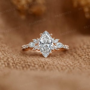 May include: A rose gold engagement ring featuring a large, marquise-cut diamond center stone. The center stone is surrounded by smaller, pear-shaped diamonds and set on a delicate band with additional small diamonds.