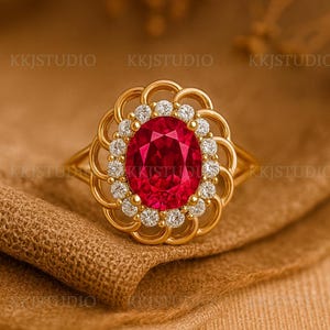 May include: A gold ring featuring a large oval-cut ruby center stone surrounded by a halo of small diamonds. The ring has a floral-inspired design and is set on a gold band. The ring is displayed on a tan fabric.
