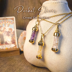 Puede incluir: Tres collares con viales de cristal dorados con piedras de diferentes colores en su interior. Los viales están suspendidos de delicadas cadenas doradas. El texto "Pocket Elixir Crystal Vial Necklace" se muestra en una elegante escritura. Una carta del tarot es visible en el fondo.