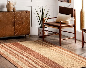 Peut inclure: Un tapis rectangulaire avec des rayures alternées beiges et brun rougeâtre. Le tapis est fait d'un matériau tissé et est posé sur un sol en bois. Le tapis est dans un salon avec un meuble en bois, une chaise et une plante en pot.