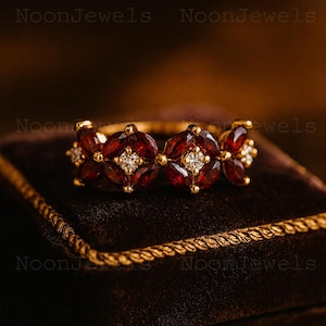 May include: A gold ring featuring a series of marquise-cut deep red garnet gemstones arranged in floral-like clusters, interspersed with small, round, clear white accent stones set in the centre of each garnet grouping.
