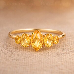 Puede incluir: Un anillo de oro con cinco piedras preciosas de citrino amarillo dispuestas en fila. La piedra central es de talla marquesa grande, flanqueada por dos piedras de talla ovalada a cada lado, montadas en una banda de oro pulido de perfil liso.