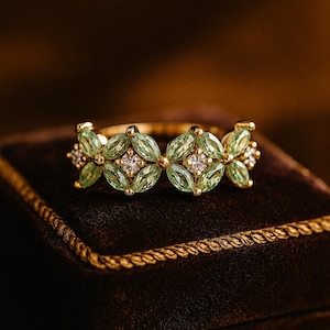 May include: A gold ring featuring a series of marquise-cut light green gemstones arranged in a floral pattern, interspersed with small, clear, round-cut stones set in the center of each cluster, creating a continuous band of faceted gems.