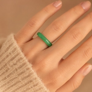 Peut inclure: Une bague anneau vert uni et lisse avec une finition polie. La bague présente un design circulaire simple et continu avec une largeur uniforme et une couleur vert émeraude translucide et vibrante, portée au doigt pour montrer son aspect épuré.
