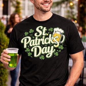 以下が含まれることがあります： 「St. Patrick's Day」の文字とビールジョッキのグラフィックが入った黒いTシャツ。シャツは緑のクローバーで飾られています。緑の帽子をかぶり、透明なプラスチックカップに入った緑色の飲み物を持っている人。