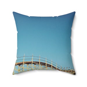 May include: A throw pillow with a photograph of a wooden roller coaster against a bright blue sky.